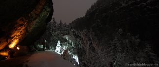 Ein Mann mit Lampe unter einem Felsen - Nachthimmel, verschneiter Wald