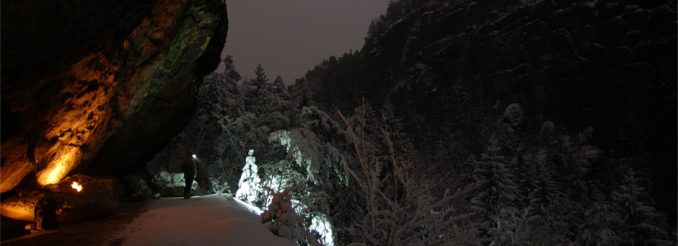 Ein Mann mit Lampe unter einem Felsen - Nachthimmel, verschneiter Wald