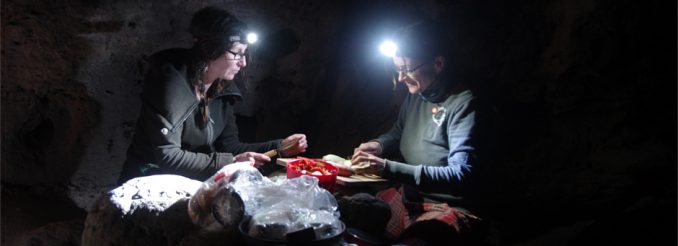 Zwei Frauen mit Stirnlampe schneiden Gemüse, dahinter Felsen