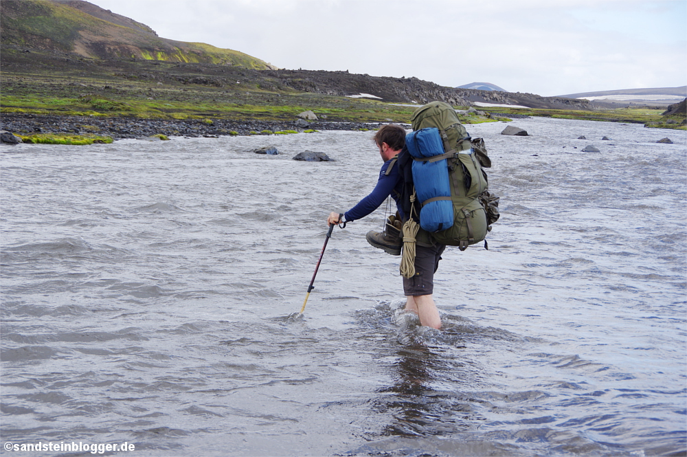 Mann watet mit Rucksack durch Fluss