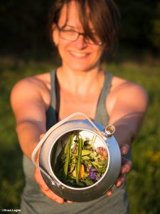 Frau mit Teekanne, in der sich Gras und Wiesenblüten befinden.