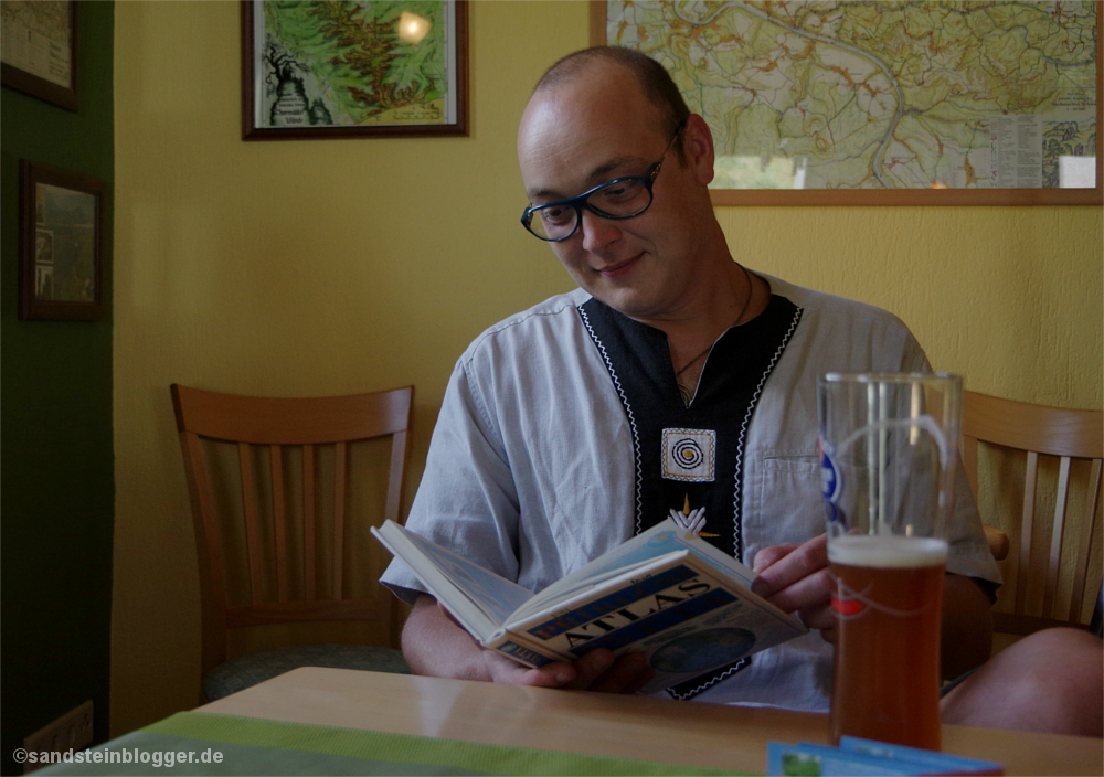 Mann mit Atlas in der Hand, im Vordergrund ein Bier.