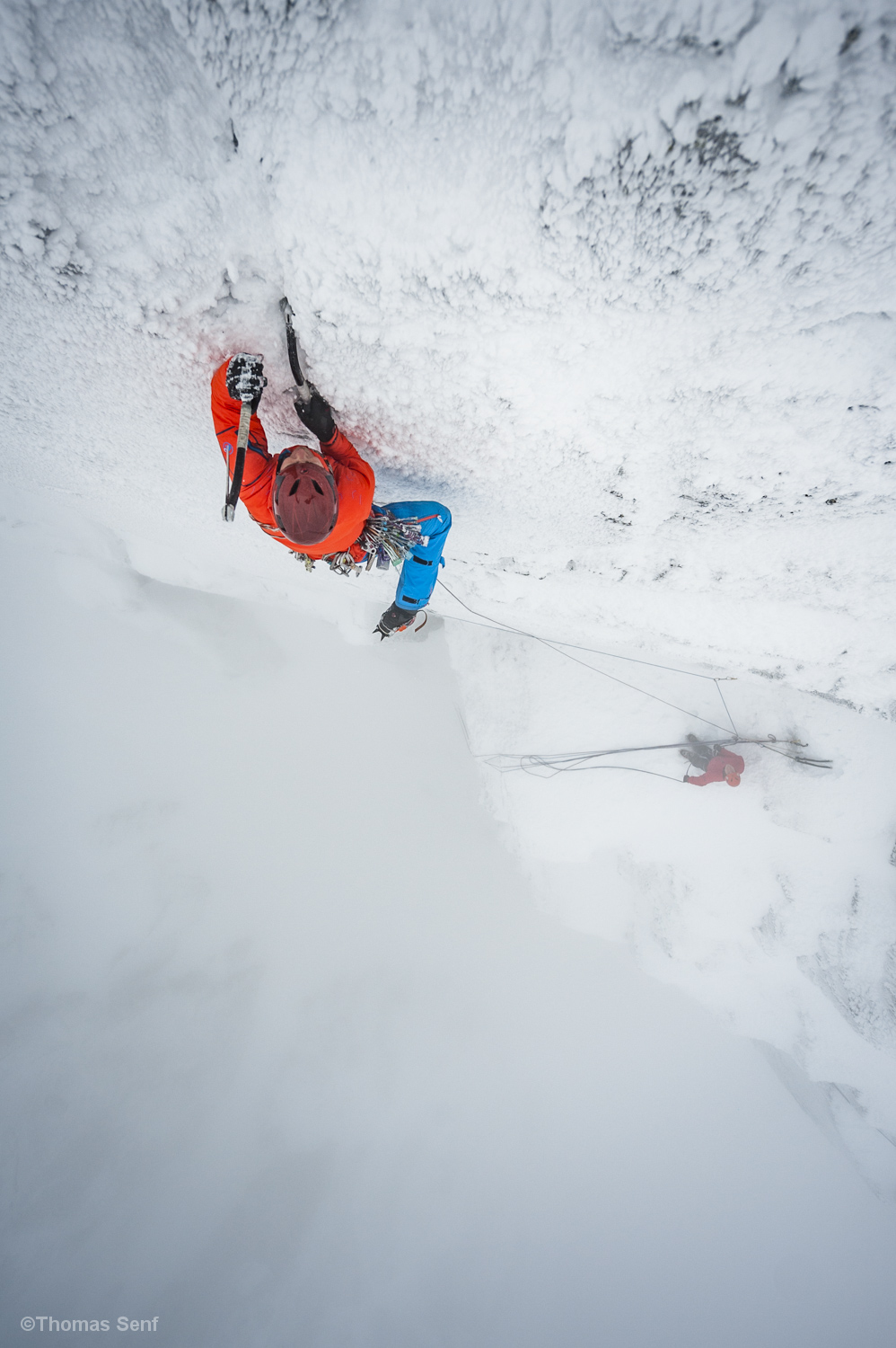 Mann klettert mit Eisäxten im Schneesturm eine vereiste Wand.