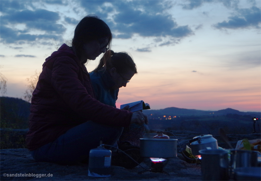 Zwei Frauen sitzen auf einem Felsplateau mit Kochgeschirr und Gaskocher