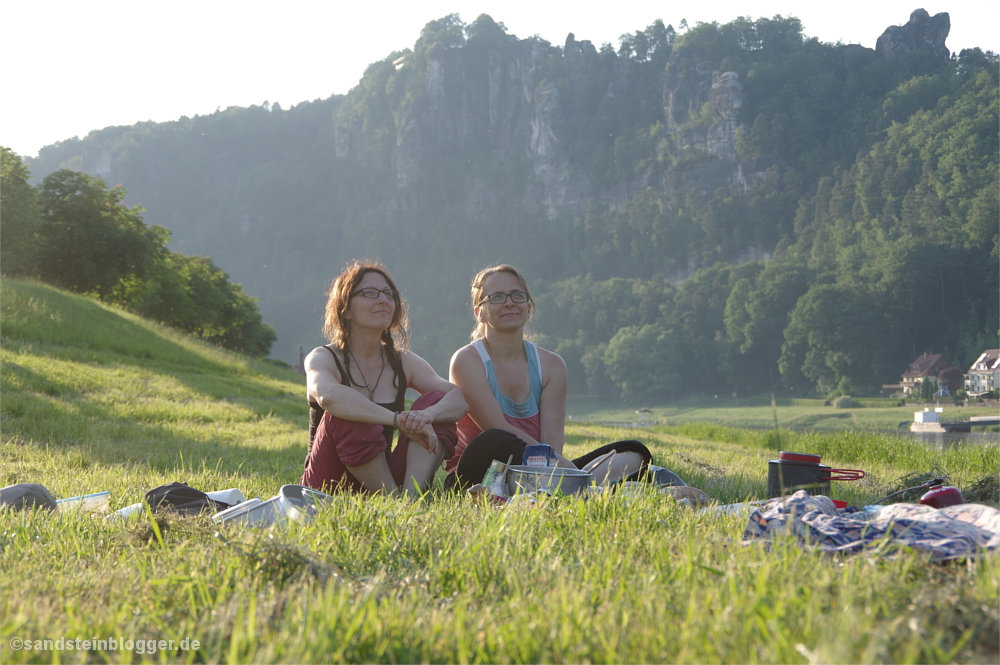 Zwei Frauen sitzen im Gras, im Hintergrund die Felsmassive bei Rathen