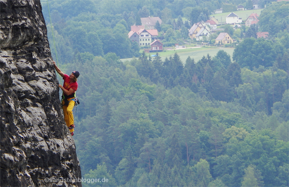 Kletterer an Sandsteinfelsen in der Sächsischen Schweiz, im Hintergrund Wälder und Häuser
