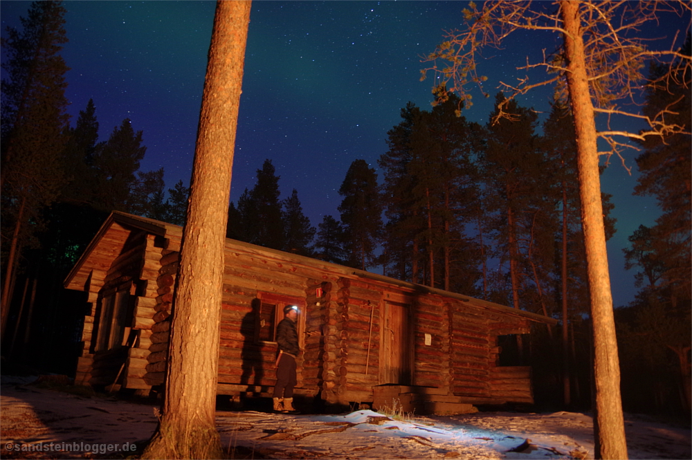 Mann mit Stirnlampe vor Blockhaus