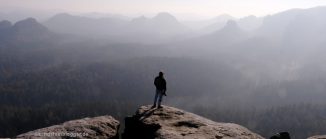 Mann auf Felsvorsprung vor Bergkulisse