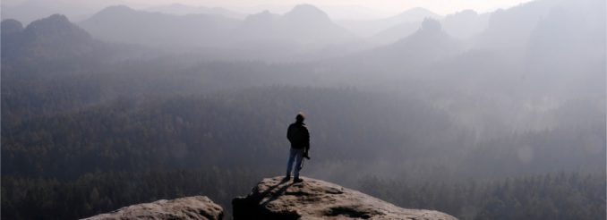 Mann auf Felsvorsprung vor Bergkulisse