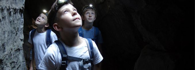 Drei Jungen mit Stirnlampe in einem Felstunnel