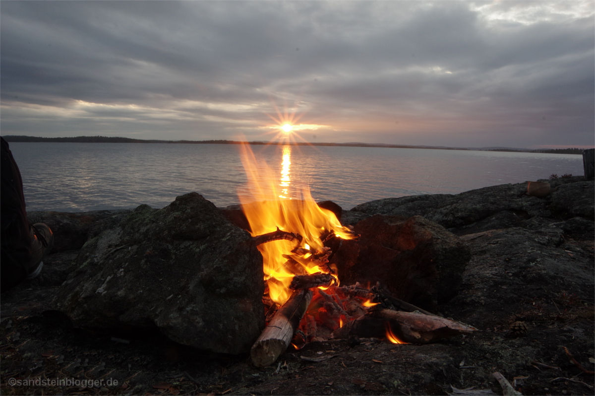 Sonnenuntergang über dem See, vorn ein Lagerfeuer