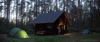 Wald, Biwakplatz mit erleuchtetem Zelt und Schutzhütte