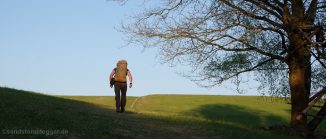 Mann mit Rucksack wandert über einen Wiesenhügel