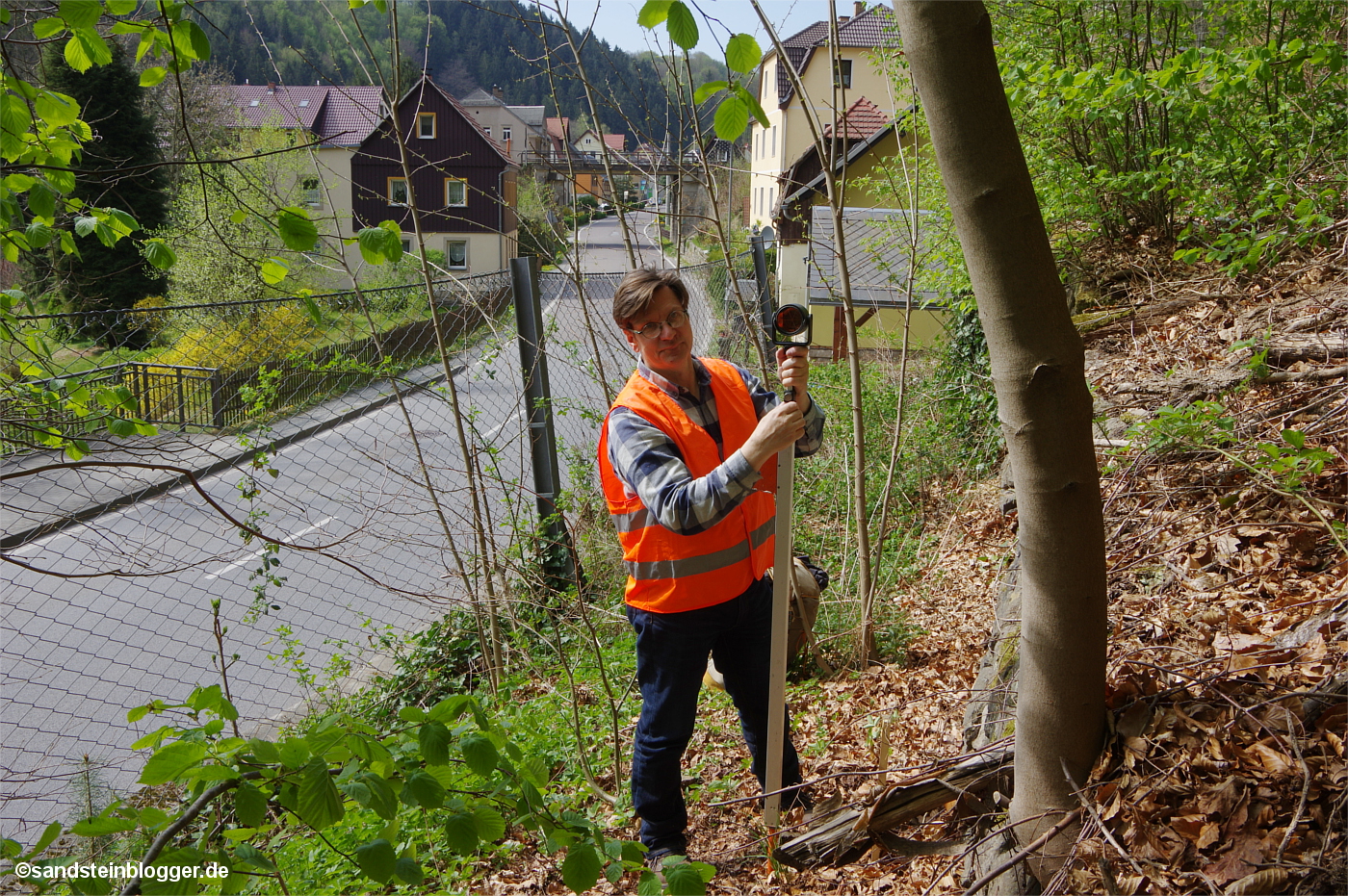 Ein Mann mit Warnweste und Vermessungsgerät an einer Straßenböschung