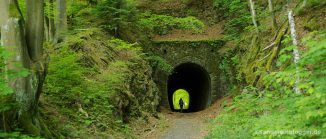 Tunneleingang versteckt im Wald - am Ende des Tunnels Licht und eine Wanderin.