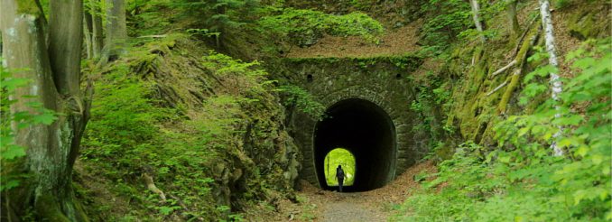 Tunneleingang versteckt im Wald - am Ende des Tunnels Licht und eine Wanderin.